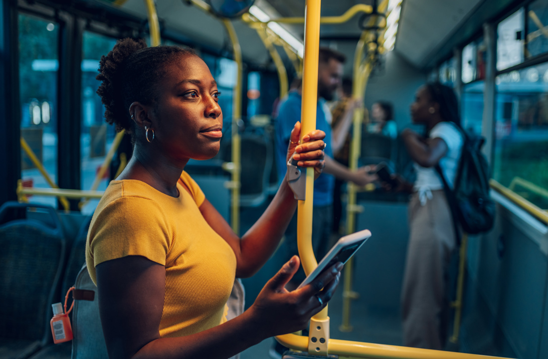 Woman in a yellow shirt and holding her cell phone while alertly standing in a bus.